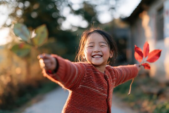 Beaming child waving fall leaves for autumn wallpaper and background design with cozy orange sweater outdoor portrait in warm golden hour light