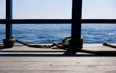 Ropes secure a dockside railing against the calm blue sea under a bright sky. © hippomyta