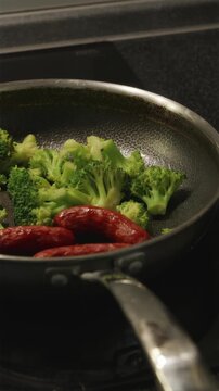 Overview of frying pan with sizzling sausages and broccoli on stovetop
