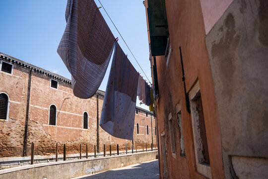 View of laundry hanging on a line between historic brick buildings in a narrow alleyway in Venice, Veneto, Italy.