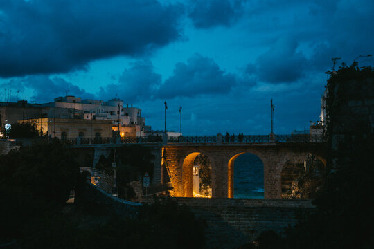 View of the historic stone bridge at Lama Monachile illuminated at night with the sea visible through its arches and buildings in the background in Polignano a Mare, Apulia, Italy.