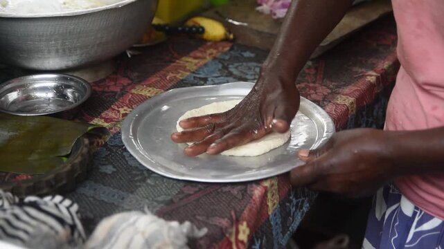 hands pressing flatbread dough on metal plate, traditional roti preparation on outdoor cooking scene, authentic culinary culture concept in slow motion taken in 60fps