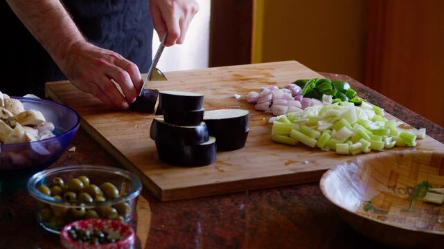 Timelapse: slicing and dicing eggplant and other vegetables to make Caponata, Sicilian specialty pickled vegetable appetizer, in contemporary kitchen, on wooden cutting board, on red granite table