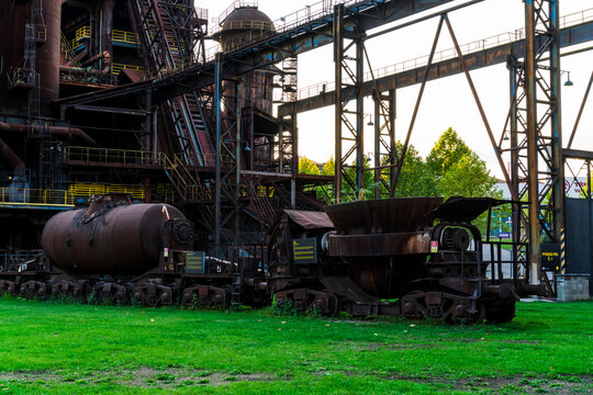 View of rusted industrial train cars, including a slag ladle car and a tank car, parked at the historic Dolni Vitkovice industrial complex in Ostrava, Moravian-Silesian Reg, Czechia.