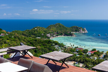 Fototapeta premium Wooden tables and chairs on an outdoor terrace overlooking a scenic tropical island view in Koh Tao, Thailand.