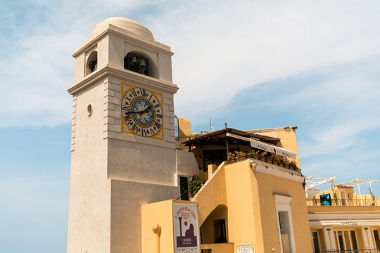 View of the historic clock tower in the Piazzetta of Capri with its distinctive yellow facade and Roman numeral clock face under a clear blue sky in Capri, Campania, Italy.