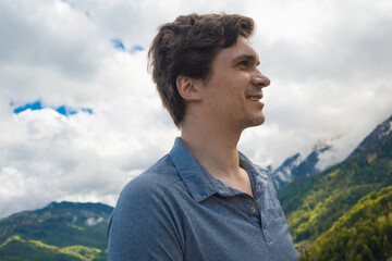 Happy young man looking at mountains, profile portrait of smiling traveler against cloudy sky © Ulia Koltyrina