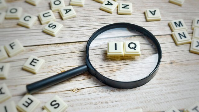 A magnifying glass placed over letter tiles spelling "IQ" on a wooden table.