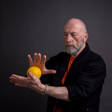 senior man is practicing reflexology therapy by rolling and pressing a spiky ball in his hands, self care and massage concept