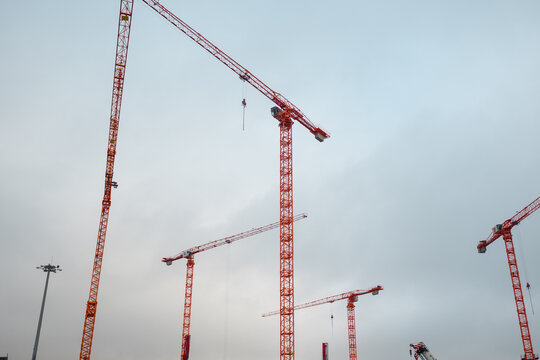 Group of red tower cranes on building site, heavy industry and infrastructure under cloudy sky