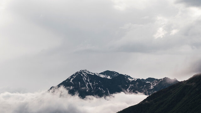 Snow-streaked peak emerging from sea of clouds, big overcast sky with copy space