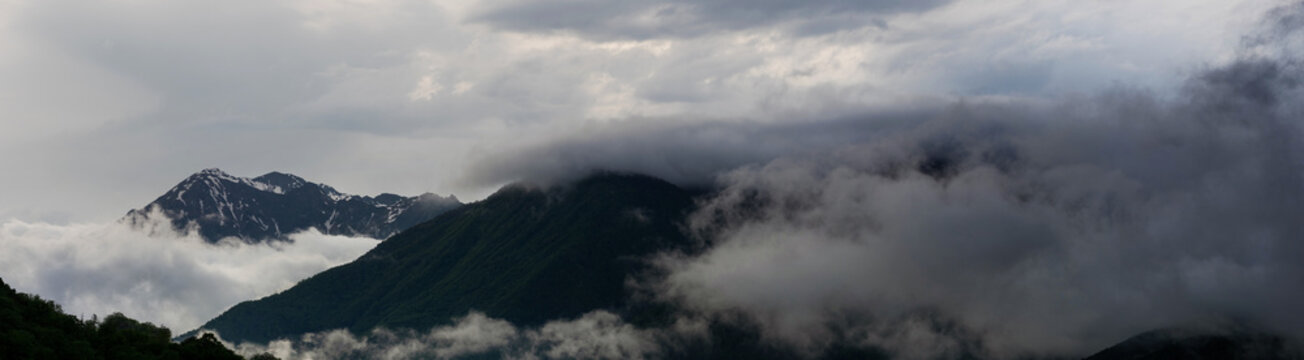 Ultra-wide panorama of storm clouds swallowing forested mountains, dramatic banner