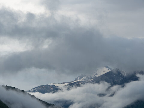 Heavy gray cloudscape over snowy peak and valley fog, dramatic sky with room for text