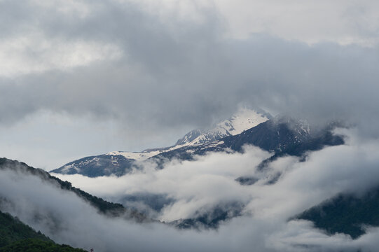 Snowy mountain peak through clouds above valley filled with fog, spring highland travel