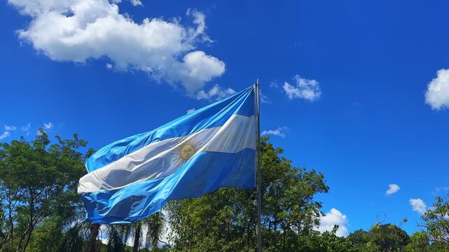 Argentine flag waving in the wind against a blue sky with white clouds in Iguazu, Argentina