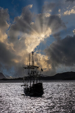 Silhouette of a traditional sailing ship beneath dramatic sun rays at sea