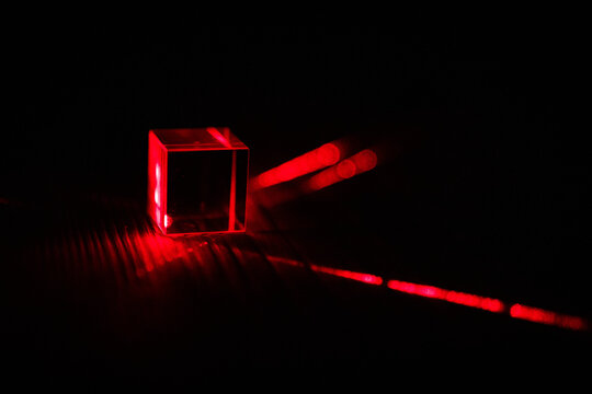 A red beam grazes the side of a transparent cube and continues onward leaving vivid points and lines that record reflection and refraction on a low key stage for conceptual science visuals