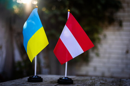 Ukrainian and Austrian desk flags stand side by side on weathered wood in warm sun with gentle bokeh signifying European partnership friendship and diplomatic dialogue between nations