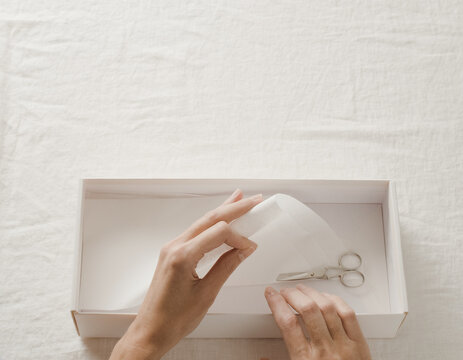 Hands folding tissue paper inside an open gift box, Black Friday packing