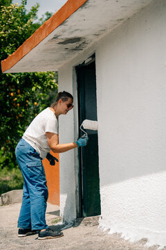 Woman Painting a Wall With Roller in Outdoor Setting