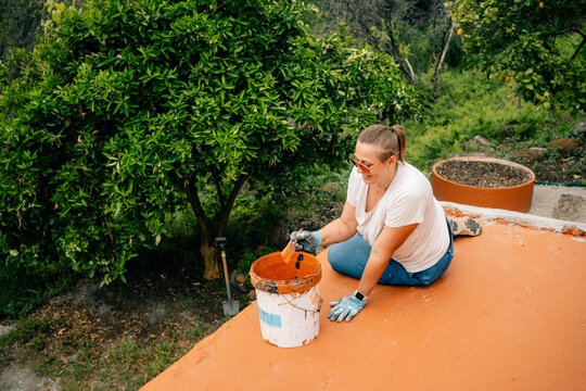 Woman Painting an Outdoor Surface in a Garden Setting