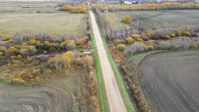 Drone looking down on autumn farmland after the crops have been harvested. A road runs through the frame
