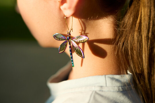 Dragonfly earring with colorful wings dangles from an ear