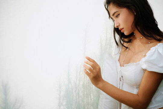 Closeup woman leaning against a white curtain and plant wall in garden
