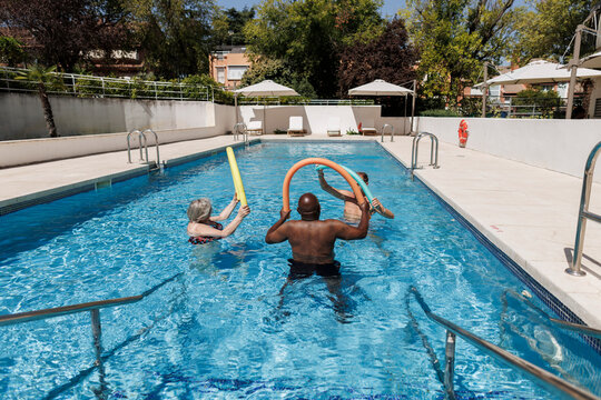 Diverse adults exercising in swimming pool with noodles