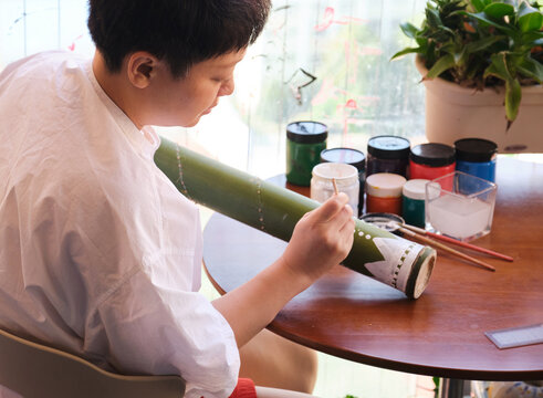Chinese female teacher hand-painting designs on a thunder tube