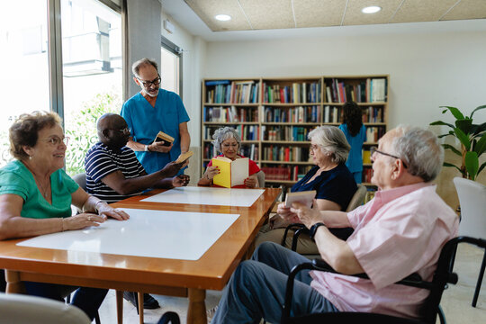 Caregiver assisting diverse senior adults reading in retirement