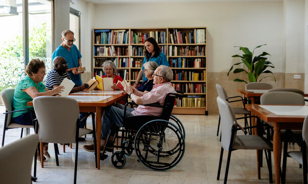 Seniors reading books with caregivers in a retirement community