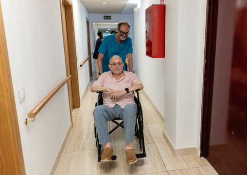 Caregiver assisting senior man in wheelchair in hospital