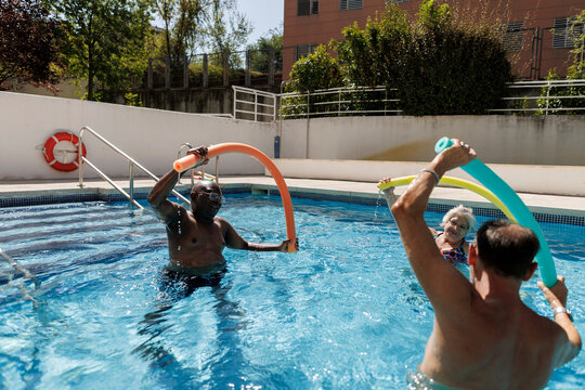 Seniors doing aqua gym exercise using pool noodles