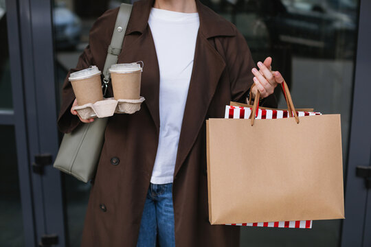 Close-up of a woman standing in a city street holding two takeaway coffees in a paper tray and three paper shopping bags