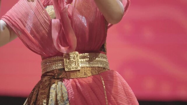 Close Up Video of an Unrecognizable Young Asian Female Singer Performing Gracefully on Stage. Wearing a Pleated Pink Top, an Intricate Golden Belt, and a Traditional Batik Skirt.