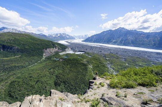 Young woman on a rocky outcrop enjoying the view, view of impressive mountain landscape with Matanuska glacier and glaciated mountain peaks, Lion's Head, Chugach Mountains, Alaska, USA