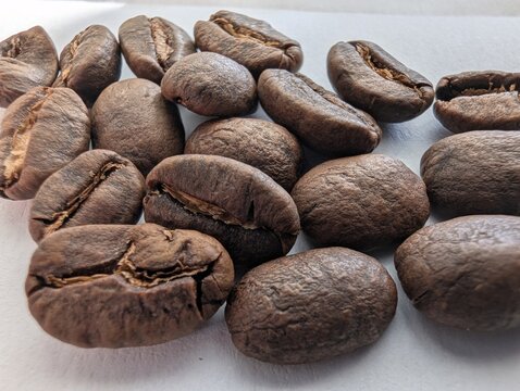 Roasted coffee beans rest on a bright white surface, their rich