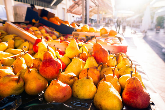 Fresh pears at the Cours Saleya food market in Nice, France, lit by the warm morning sun of the Mediterranean Sea, with stalls and customers in the blurred background