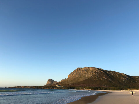 Distant side view of a surfer on a wide sandy beach with Hangklip Mountain and Cape Point in the distance, Pringle Bay Beach, Cape Town, Western Cape, South Africa