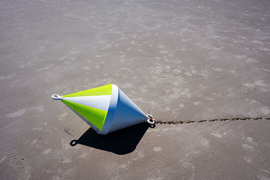 A yellow anchor buoy lies on the North Sea beach at low tide.