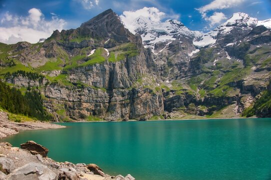 Turquoise waters of Oeschinen Lake backed by the towering rocky cliffs of the Bernese Alps near Kandersteg, Bernese Oberland, Switzerland