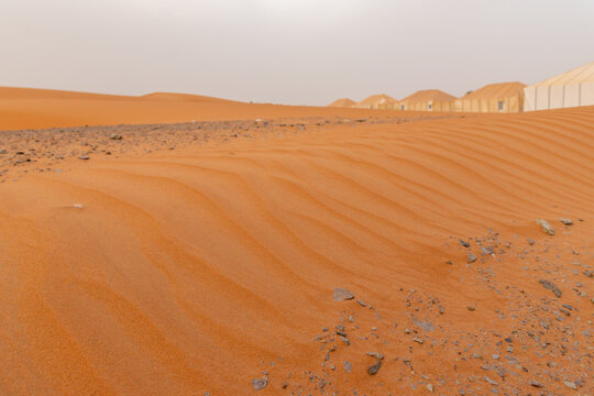 Rippled orange sand dunes with a row of tents in the distance, Sahara desert, Merzouga, Draa-Tafilalet region, Errachidia Province, Morocco