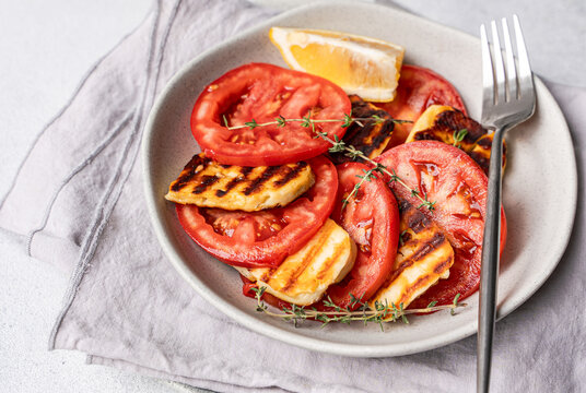 Close-up of a sliced tomato and grilled halloumi cheese salad with lemon and thyme