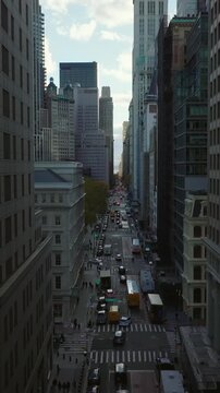 Vertical video: Backwards reveal of one way street between tall city buildings. Construction site aside road. Manhattan, New York City, USA