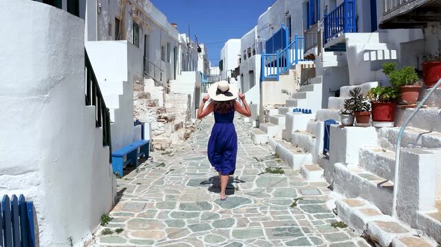 A tourist woman in a blue dress explores the whitewashed old town Kastro of Folegandros island, Cyclades, Greece