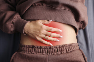 Naklejka na ściany i meble Woman with hand on painful lower abdomen. Red highlighted stomach area for abdominal discomfort. Belly pain and cramp concept background. Female body close up. Digestive health problem.