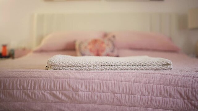 An upholstered bench stands before a pink bed with a knitted throw blanket. Bedroom interior. Cozy home comfort.