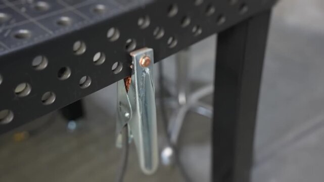 Close-up of gloved hand stripping copper wire and exposing conductor strands over perforated metal workbench during electrical assembly in industrial workshop