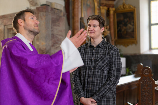 A young man student engages in conversation with a catholic priest inside a church, discussing religious topics related to christian faith.